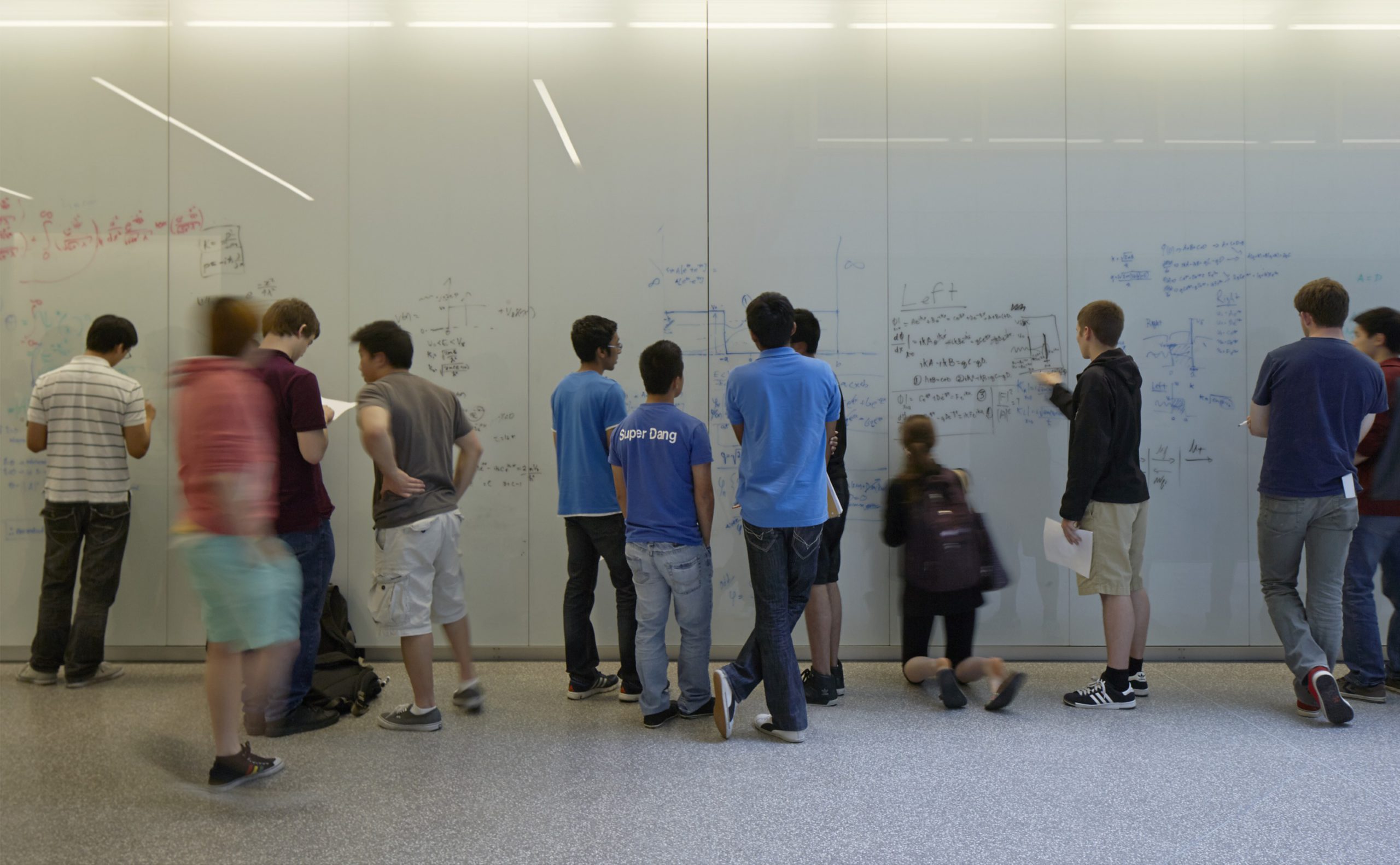 students writing on whiteboard wall